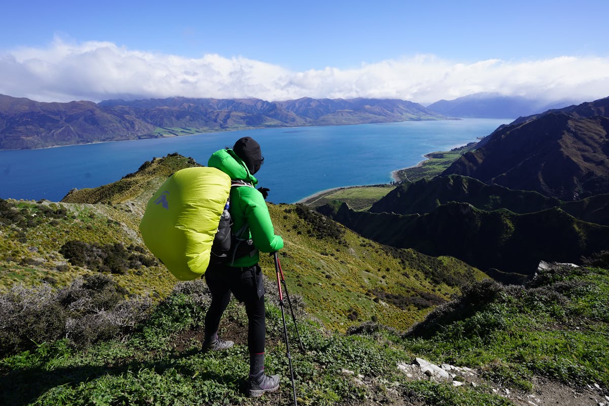 Hiker with trekking poles enjoying panoramic view of a lake and mountains in New Zealand