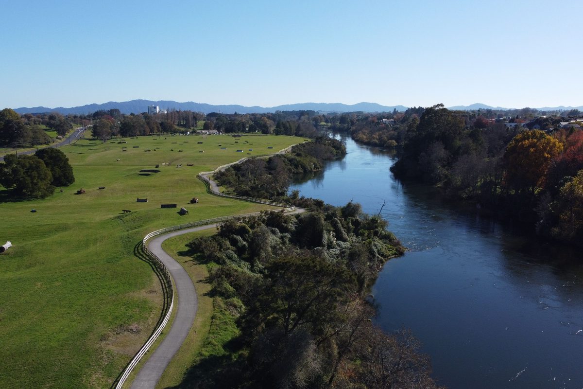 Aerial view of a river winding past parkland and a paved riverside path