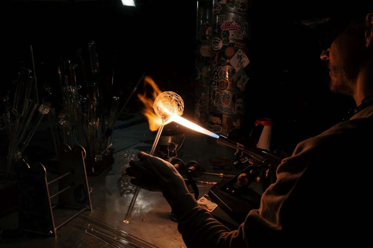 Artisan shaping molten glass with a torch in a darkened glassblowing studio